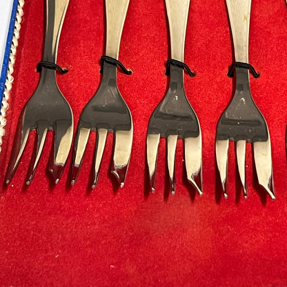 Close-up of a red and blue box containing 12 French dessert forks on a white background