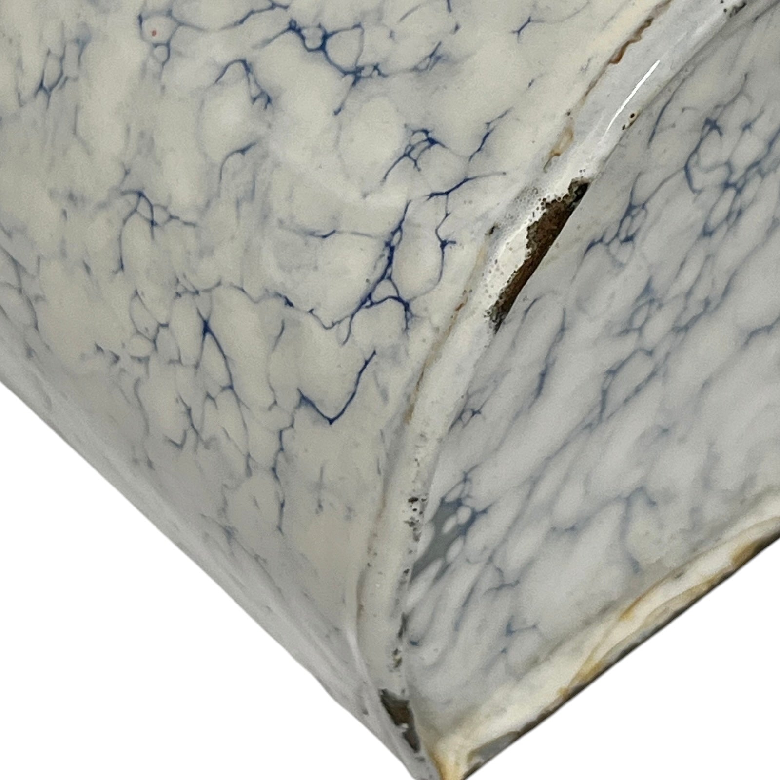 Close-up of a white marble-patterned surface with blue veining and a curved edge showing a dark interior.