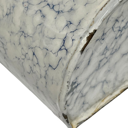 Close-up of a white marble-patterned surface with blue veining and a curved edge showing a dark interior.