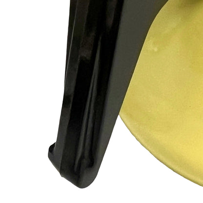 Close-up of a glossy black curved object next to a yellow circular surface on a white background.