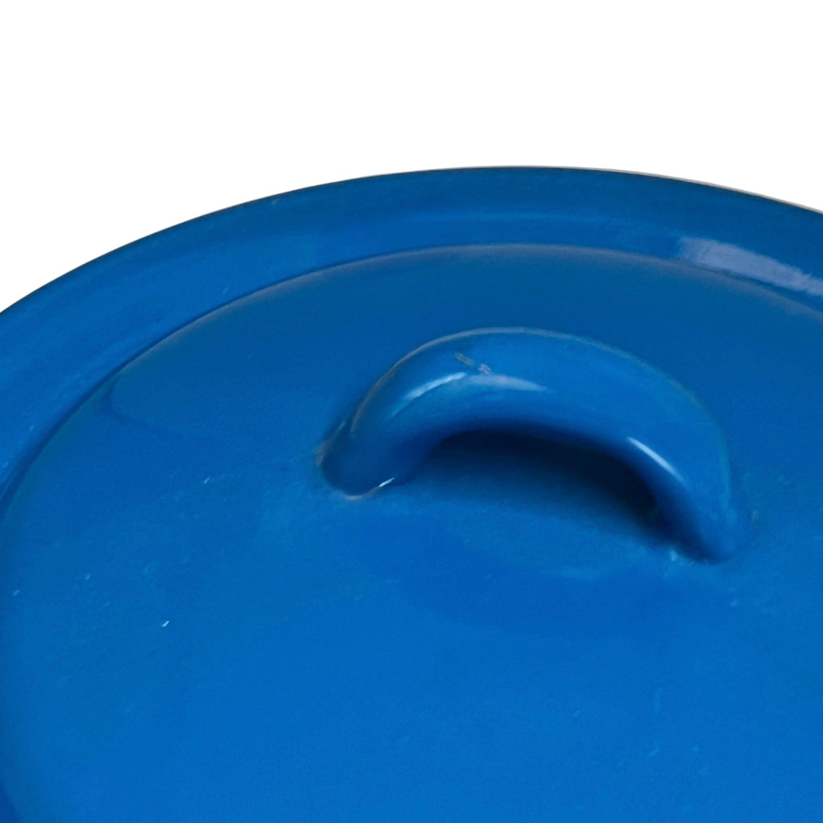 A close-up of a bright blue round lid with a raised arched handle, photographed against a white background.
