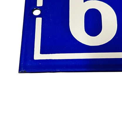 Close-up of a blue square sign or plaque with a white border and large white letter 'b' visible, showing a small mounting hole near the top left, on a white background.