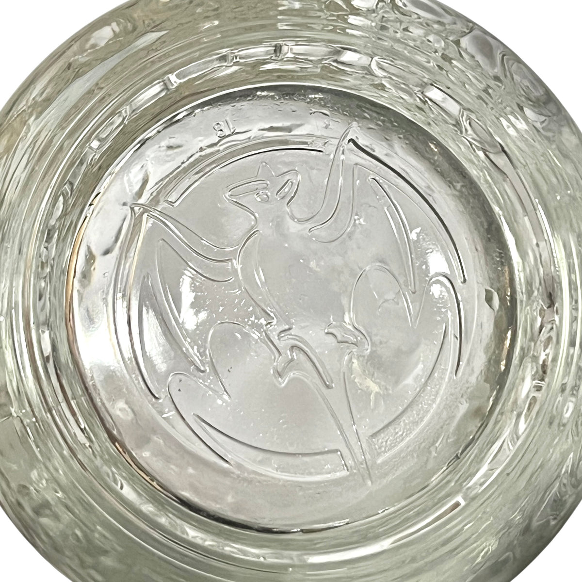 A close-up of a clear glass bowl or dish with a raised embossed bat design in the center and a textured, ribbed rim.