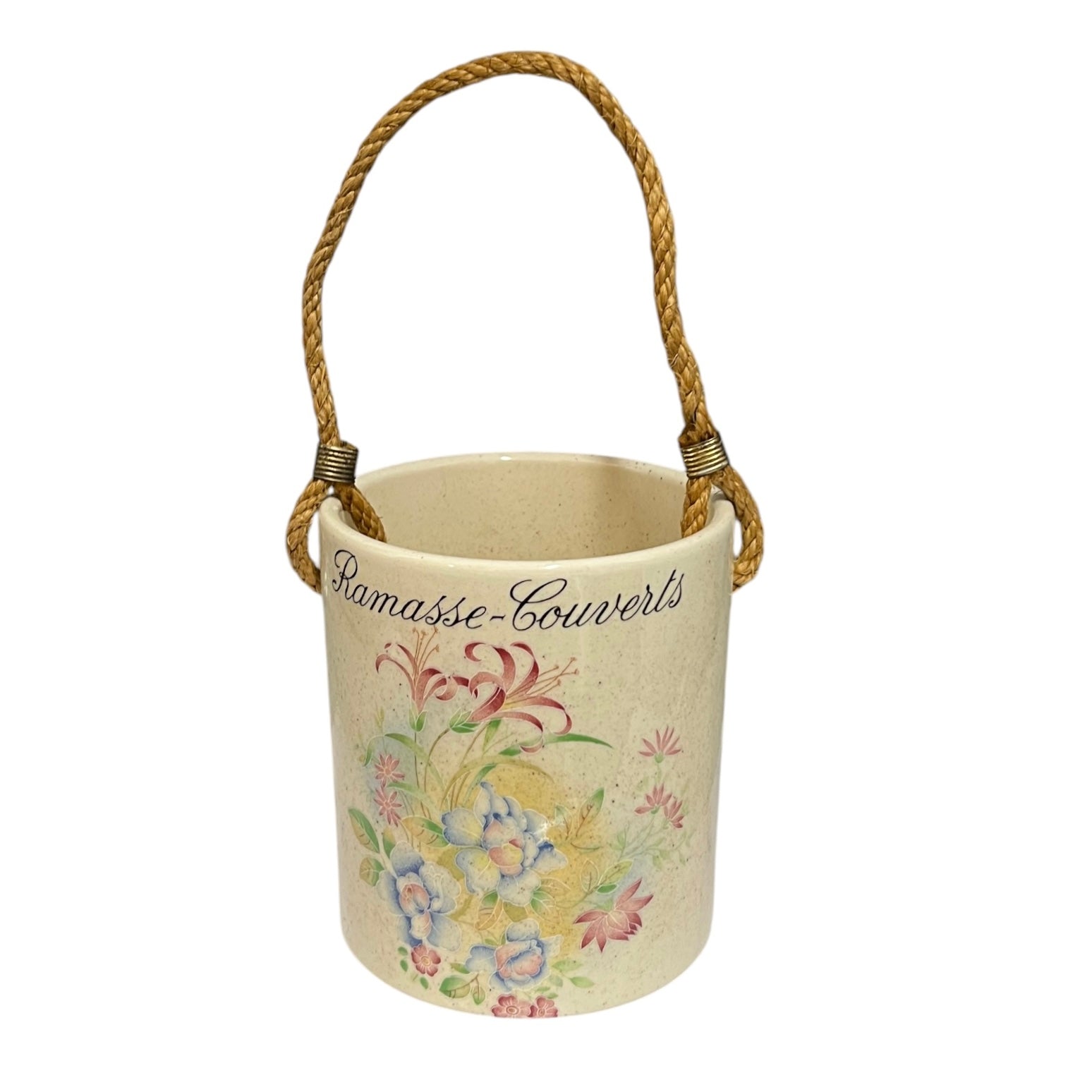 A cylindrical ceramic utensil pot in a warm cream colour, decorated with a colourful floral pattern and the French text 'Ramasse-Couverts' in black script. It features a natural jute rope handle wrapped with small metal connectors, set against a plain white background.