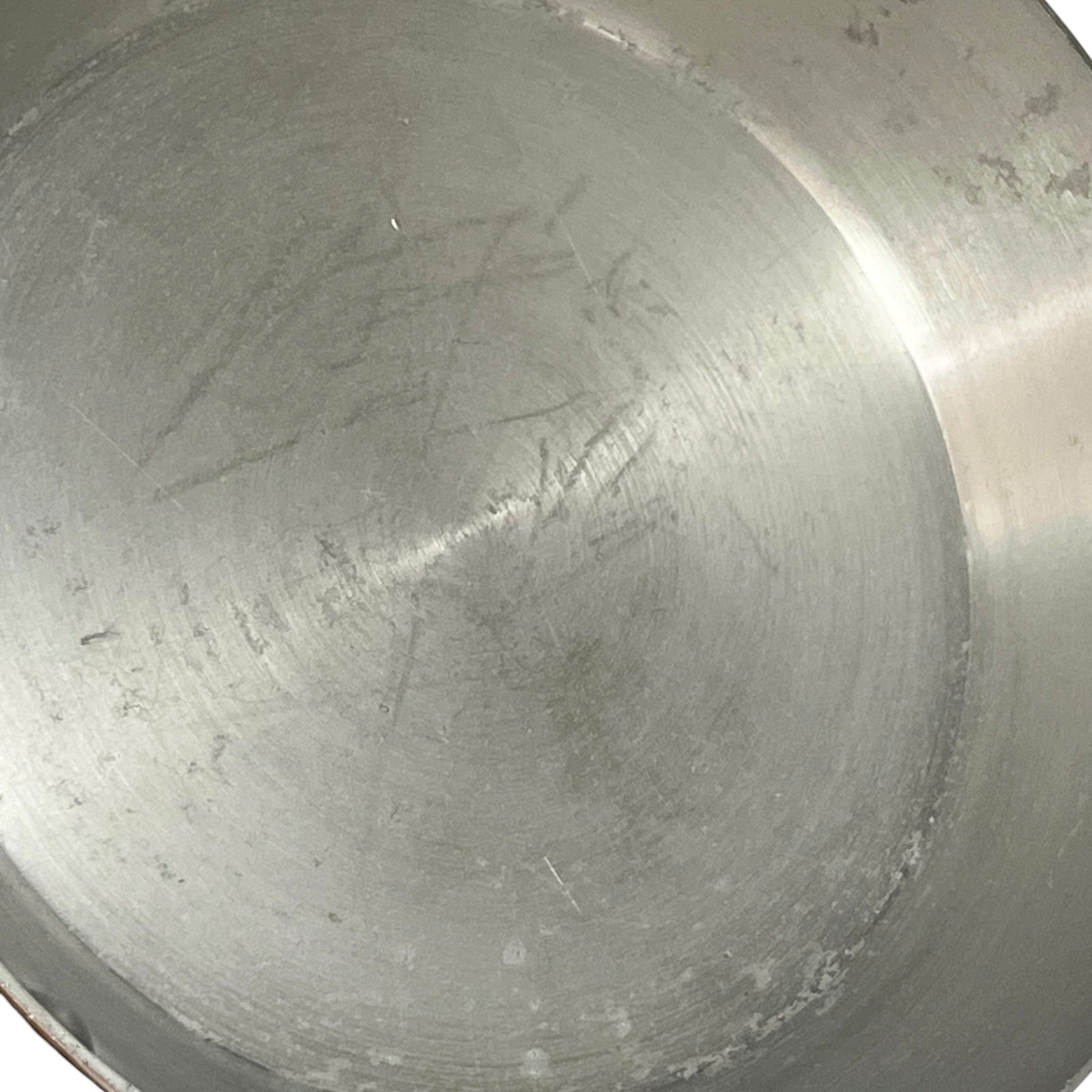 Close-up of the inside of a brushed metal pot or pan showing a scratched stainless steel surface.