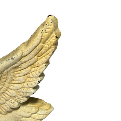 A close-up of a textured angel wing sculpture in a warm cream or beige tone with dark speckles, shown against a plain white background.