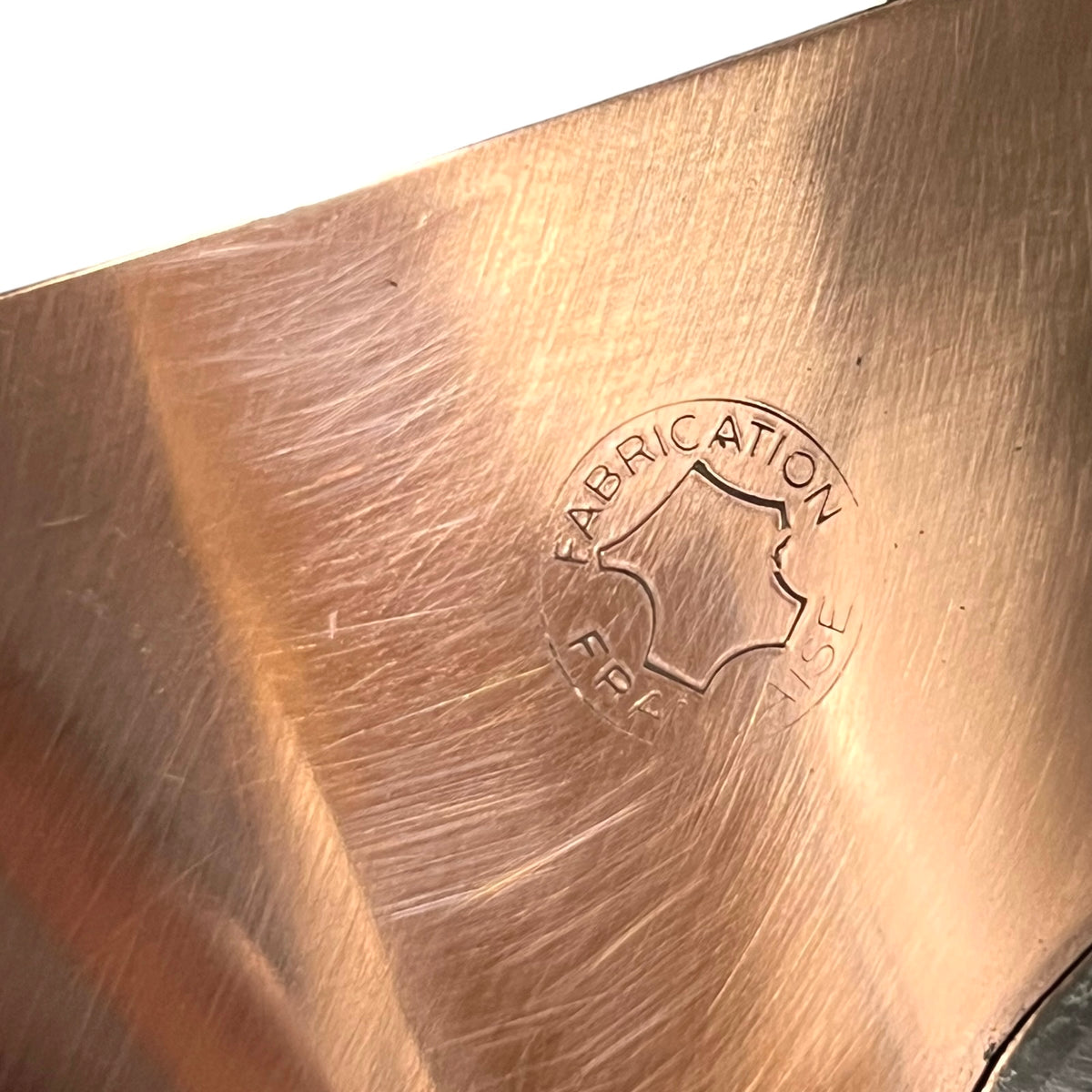 Close-up of a brushed copper-colored metal surface with a stamped circular logo reading FABRICATION FRANCAISE.
