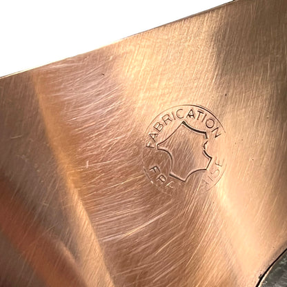 Close-up of a brushed copper-colored metal surface with a stamped circular logo reading FABRICATION FRANCAISE.