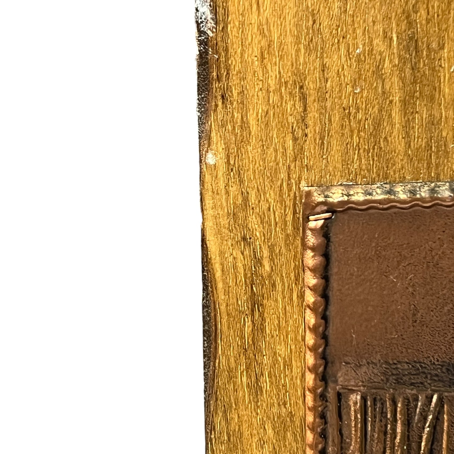 Close-up detail of a wooden panel with a copper inlay patch bordered by a metallic bronze-toned frame, shown against a white background.