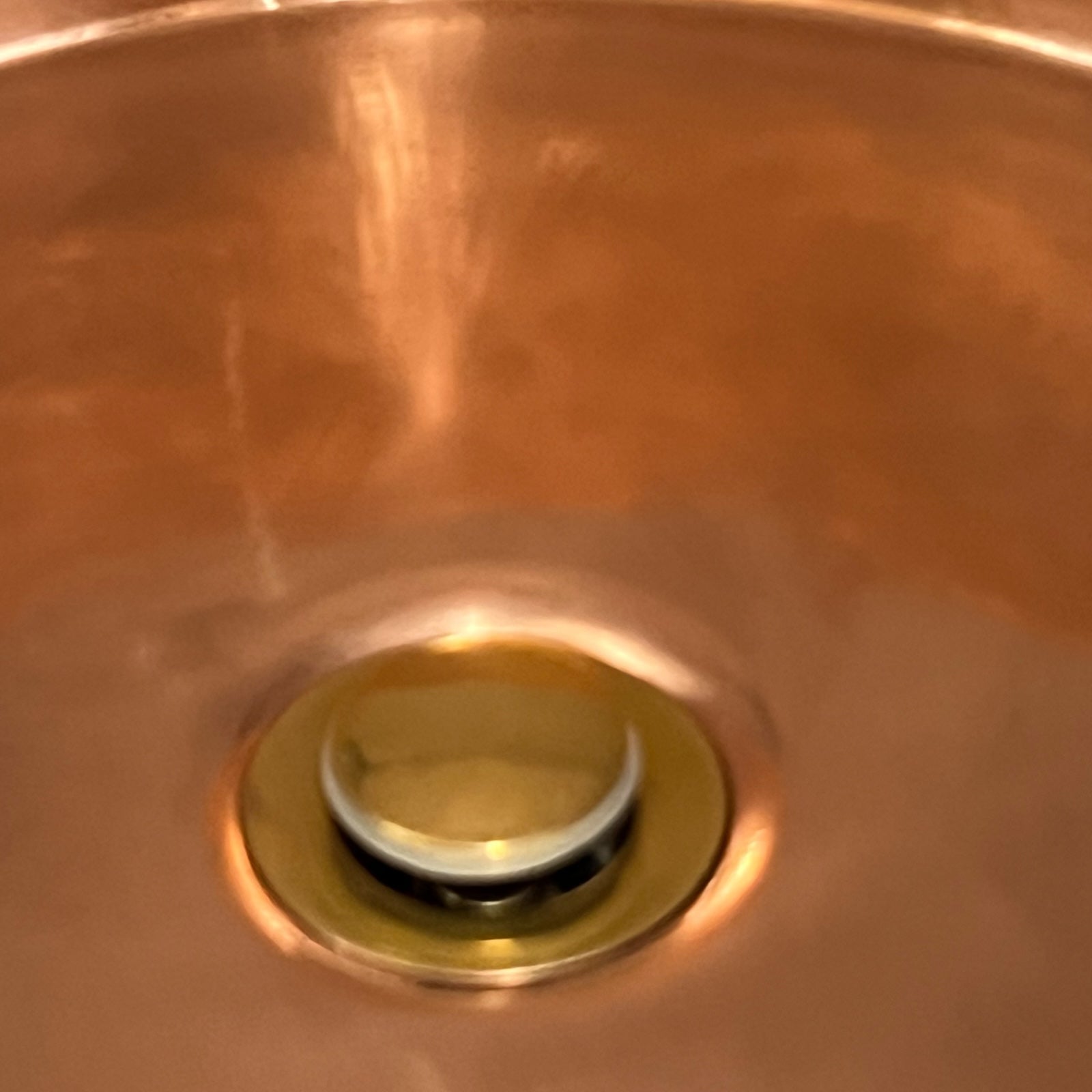 Close-up of copper sink with brass pop up waste on a white background