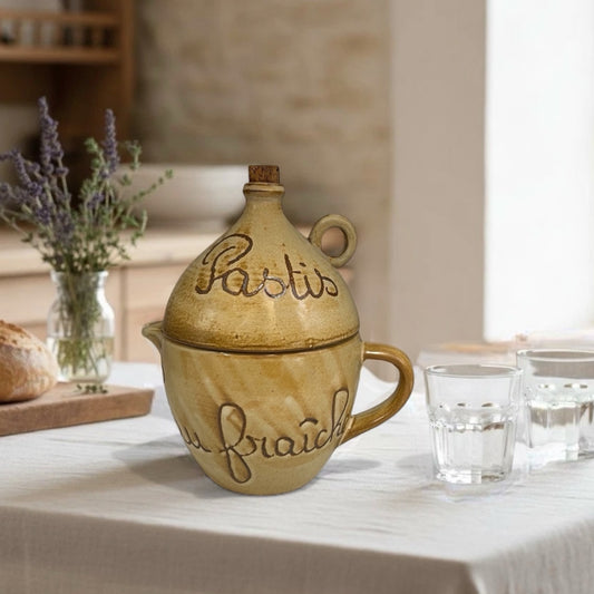 Decorative ceramic jar with 'Pastis' text on a table with glasses and bread.