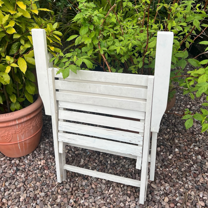 A French vintage wooden slatted folding garden chair set in a charming garden with a greenhouse, potted plants, and a gravel path, perfect for creating a rustic country cottage vibe.