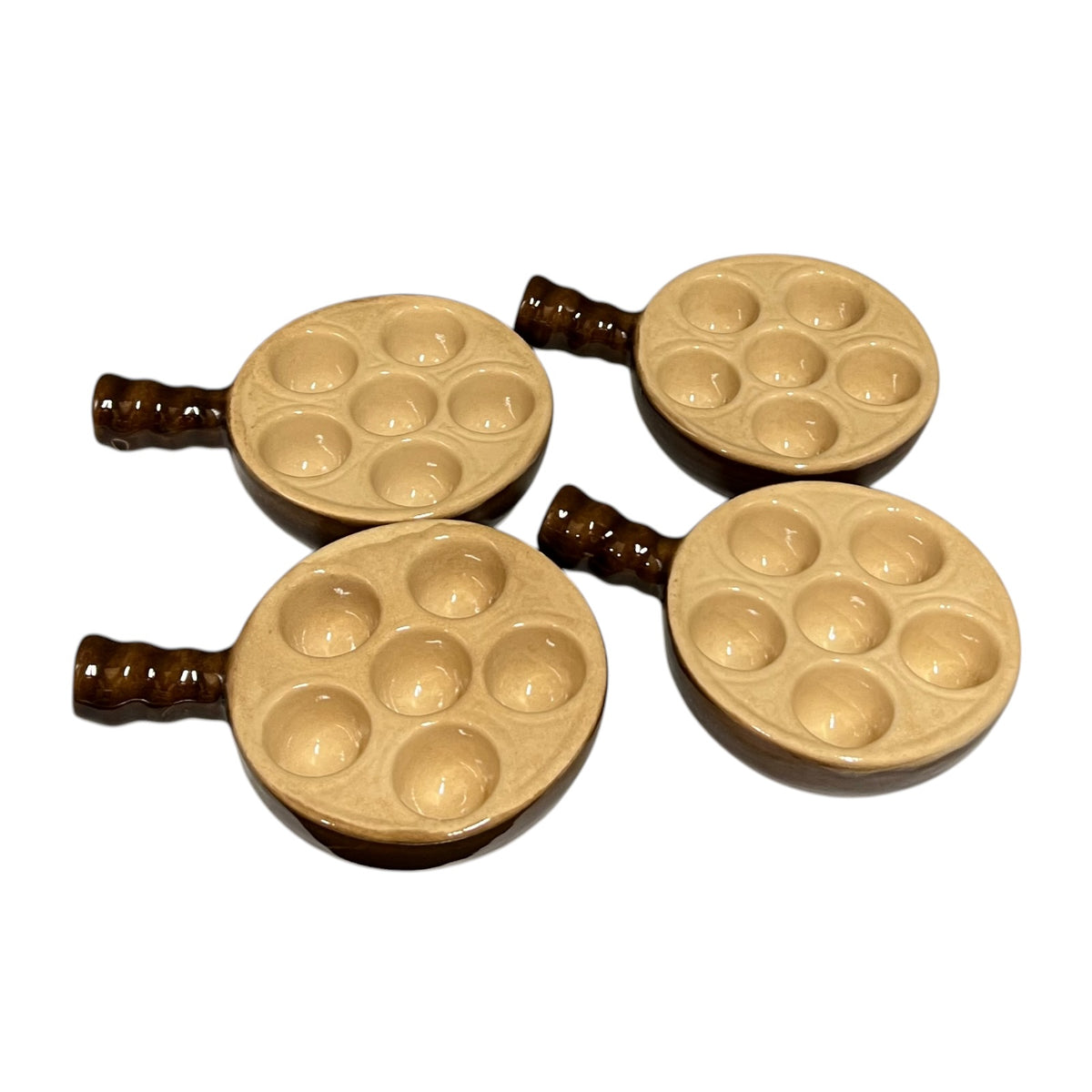 Four small ceramic escargot dishes with six shallow round wells and dark brown handles, arranged on a plain white background.