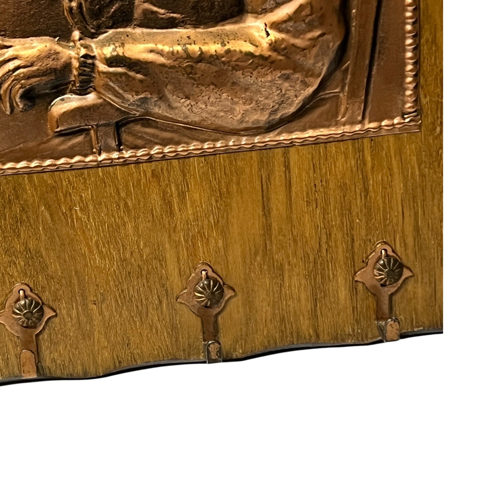 Close-up of a decorative wall-mounted wooden panel with a bronze-toned relief figure at the top and four matching metal hooks along the lower edge, shown against a white background.