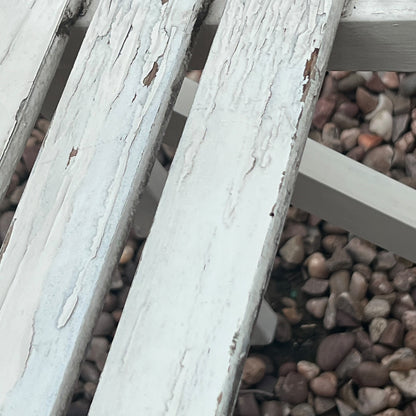 A close-up view of a painted wooden slatted garden chair set amidst a lush garden backdrop.