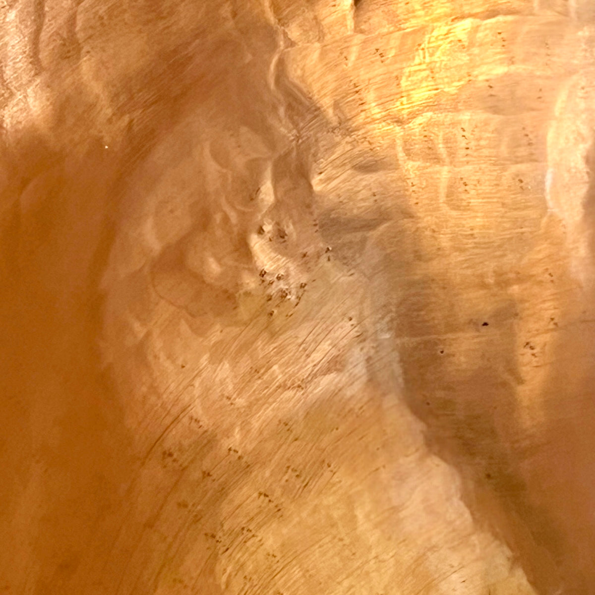 A close-up of a warm, textured copper sink with swirling golden-brown and amber tones, resembling polished wood, copper, or a metallic finish.