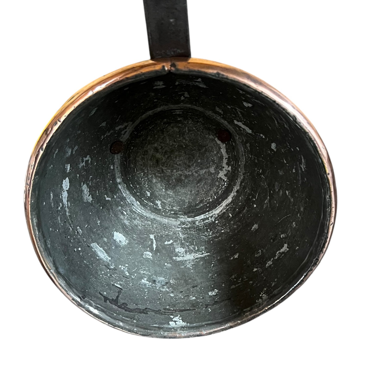An overhead close-up of the interior of a dark metal pot or pan with a copper-toned rim and a black handle, shown against a plain white background.
