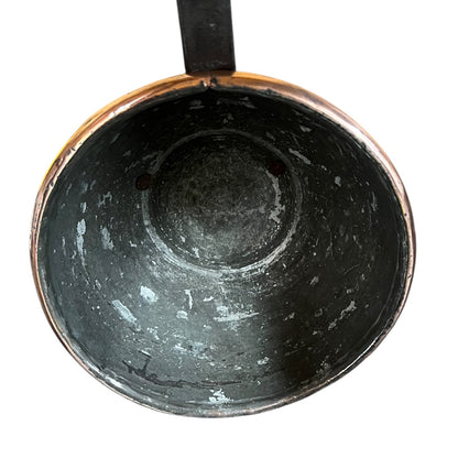 An overhead close-up of the interior of a dark metal pot or pan with a copper-toned rim and a black handle, shown against a plain white background.