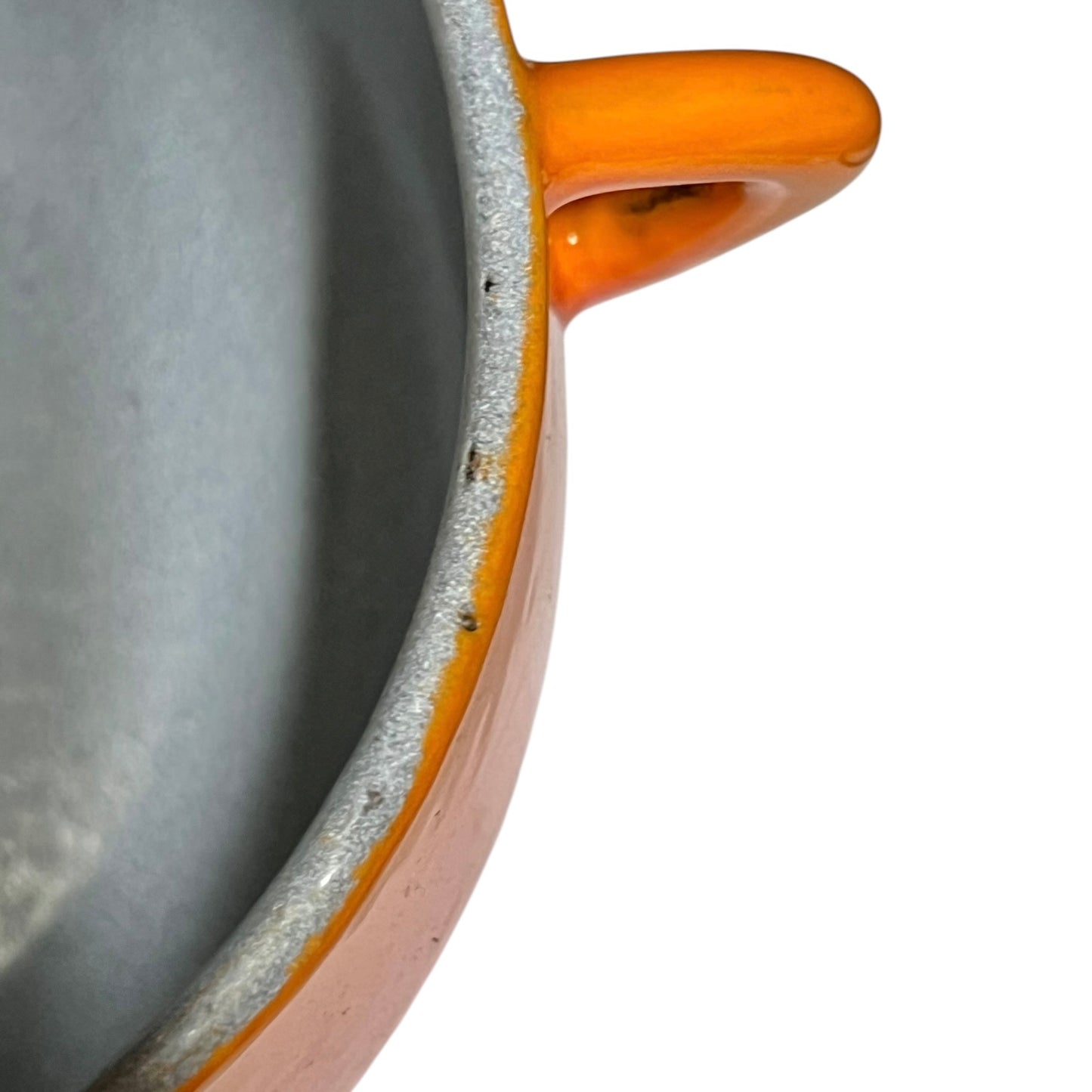 Close-up of a ceramic pot or casserole dish corner showing a matte gray interior, a speckled off-white glazed rim, and a glossy orange-brown handle on a white background.