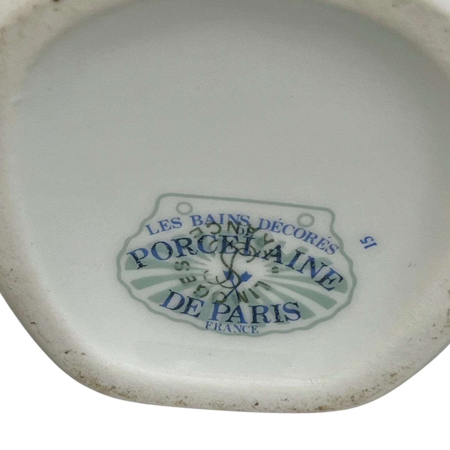 The bottom of a white porcelain dish or plate with a blue and green printed label reading 'LES BAINS DÉCORÉS PORCELaine DE PARIS FRANCE'.