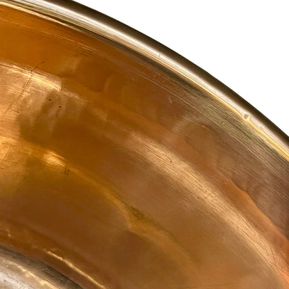Close-up of a metallic copper-colored bowl or pot interior with a brushed finish and a white background visible at the top right.