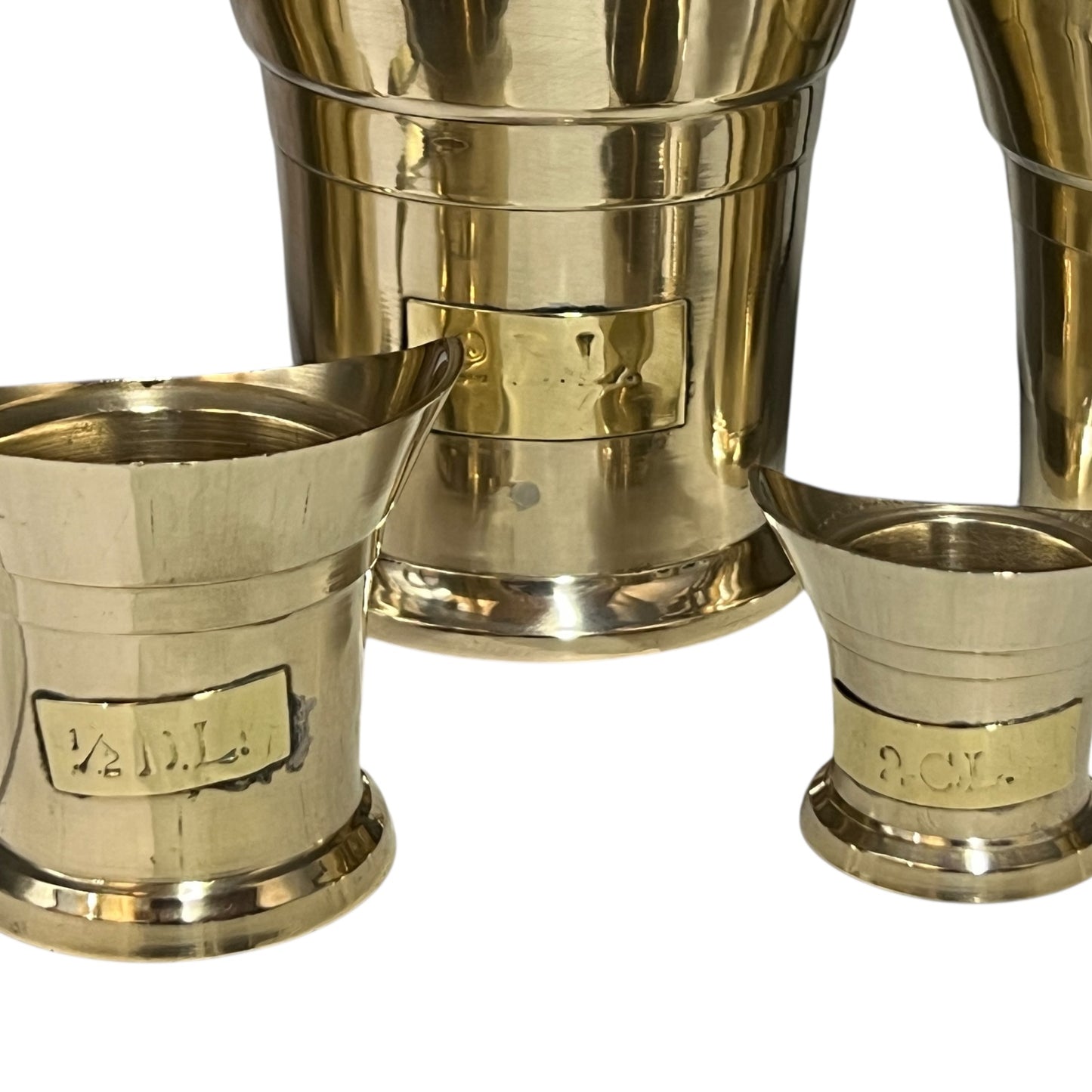 Three brass measuring cups with engravings on a white background