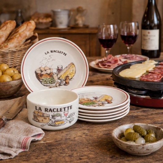La Raclette ceramic dishes and bowls on a wooden table with wine and food.