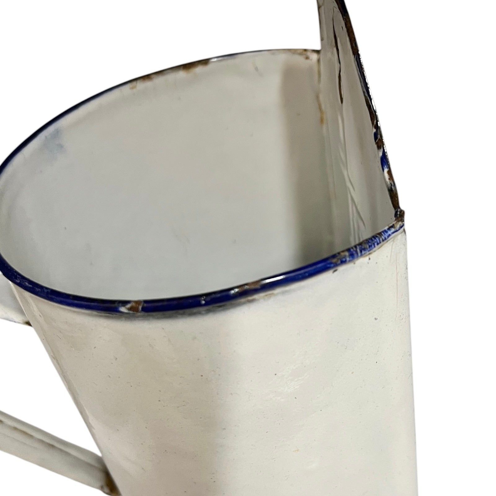 A close-up of a vintage white enamel pot with a blue rim and a distressed, weathered finish.