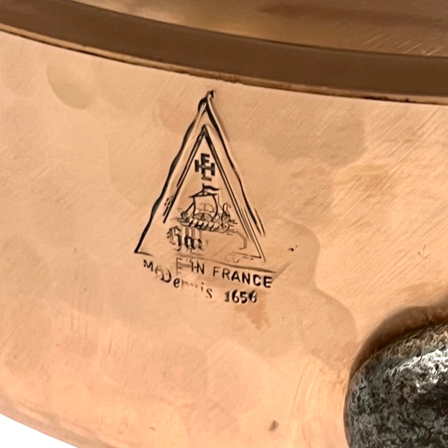 Close-up of a copper pan with a engraved logo and text on a white background