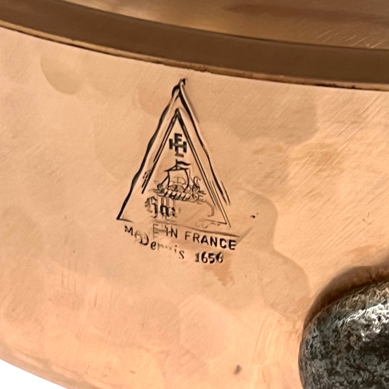Close-up of a copper pan with a engraved logo and text on a white background
