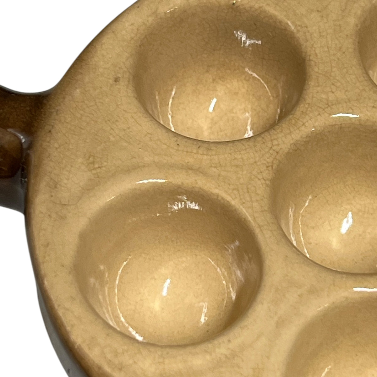 Close-up of a ceramic escargot plate with multiple circular wells and a glossy finish, showing a warm beige glaze.