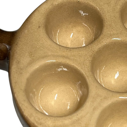 Close-up of a ceramic escargot plate with multiple circular wells and a glossy finish, showing a warm beige glaze.