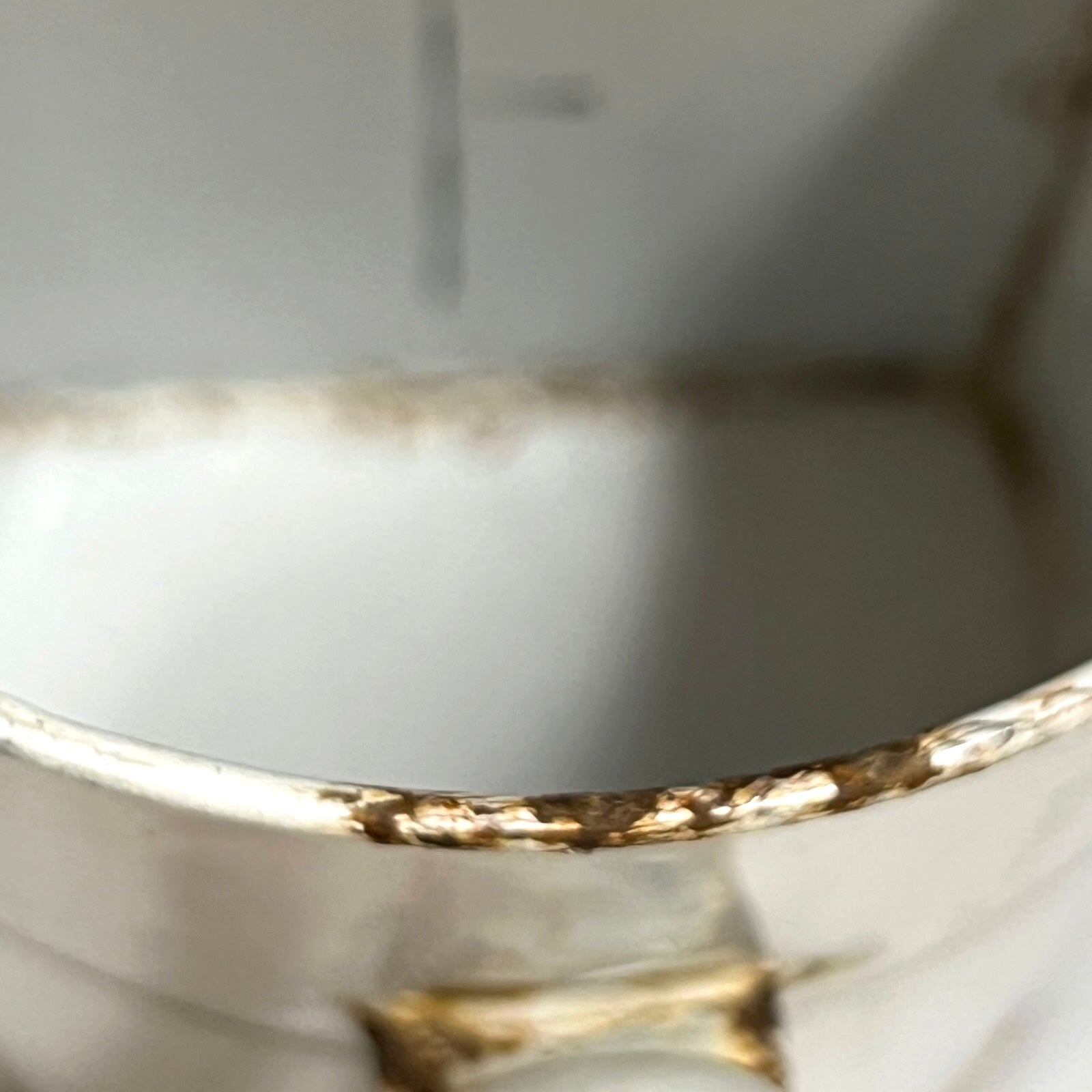 Close-up of the rim of a white pot showing heavy brown rust or mineral buildup along the edge.