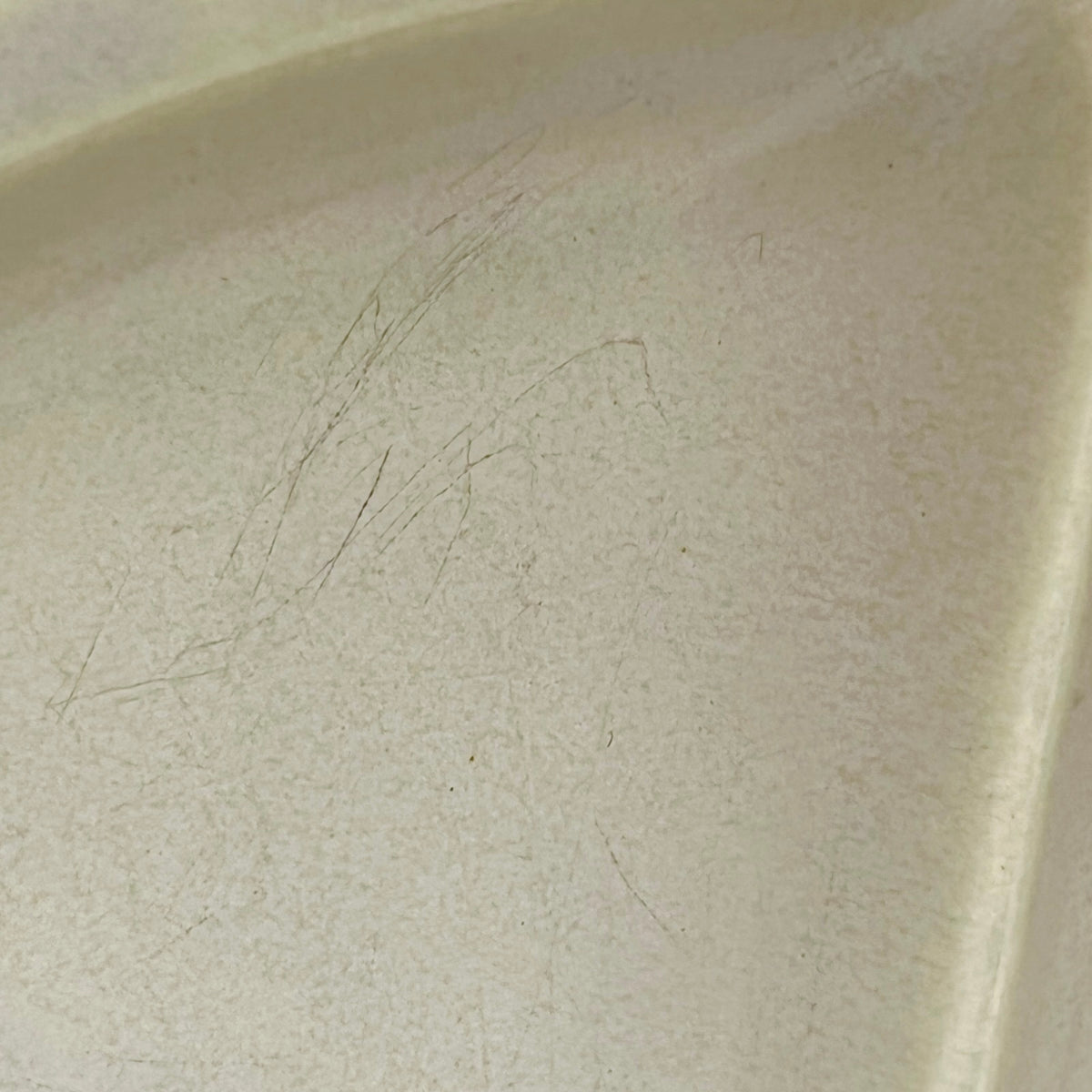 Close-up of a light beige ceramic surface with visible scratches and wear on the interior corner.