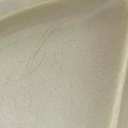 Close-up of a light beige ceramic surface with visible scratches and wear on the interior corner.
