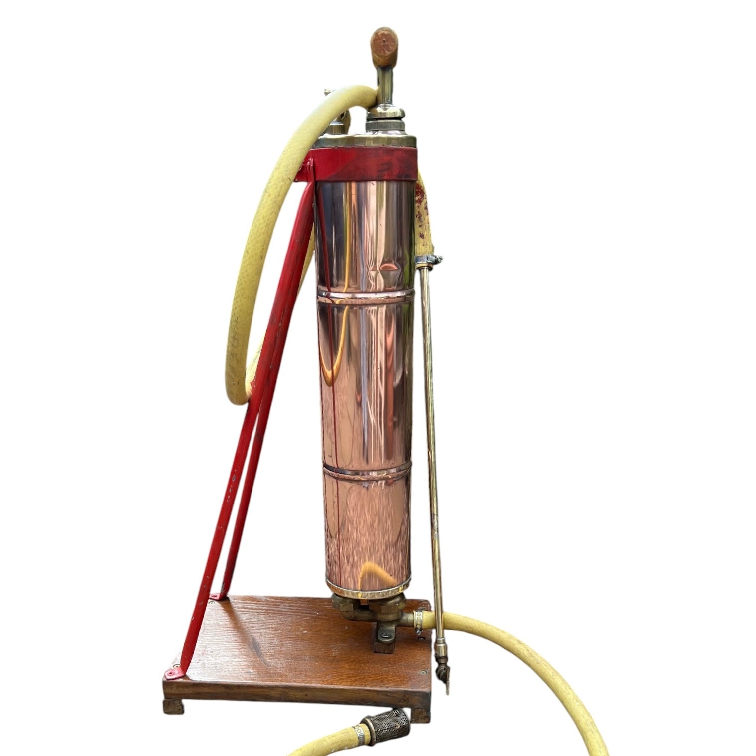 French vintage copper garden sprayer with a yellow hose and nozzle, standing upright on a wooden mount with a red-painted metal bracket. A wooden handle for pumping sits at the top, making it ideal for a vintage garden, all set against a white background.