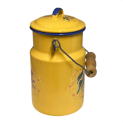 A vintage yellow enamel milk canister with a matching lid, featuring hand-painted floral motifs and a metal handle with a cork grip, isolated on a white background.