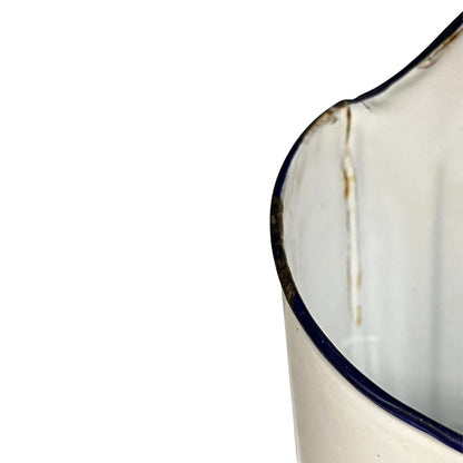 Close-up of a white enamel jug with a dark blue rim, showing a vertical stain or chipped area on the edge against a white background.