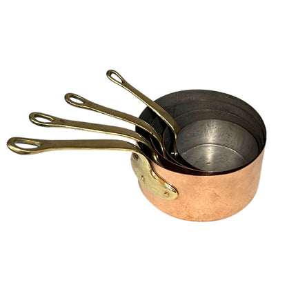 Set of four copper saucepans with brass handles on a white background