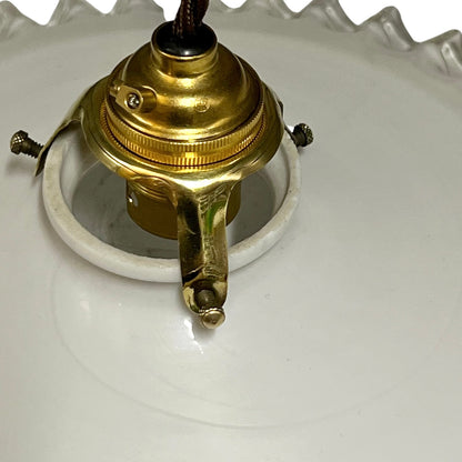 A close-up of a vintage brass ceiling light fixture socket and canopy assembly attached to a white ceramic lamp shade.