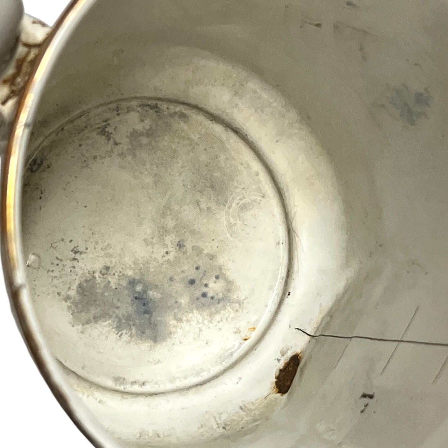 Close-up view inside a white enamel pot showing the bottom interior with some staining, scuffs, and a small dark spot near the rim.