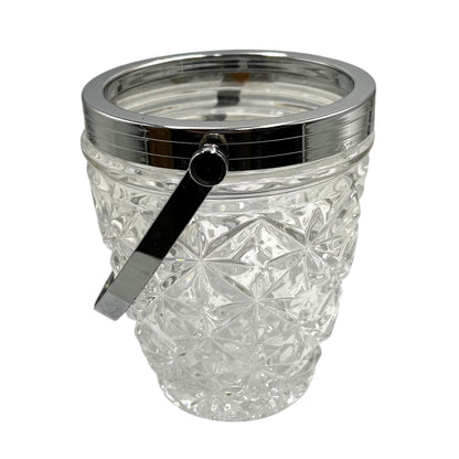 Clear French cut glass ice bucket with textured design and metal handle on a white background