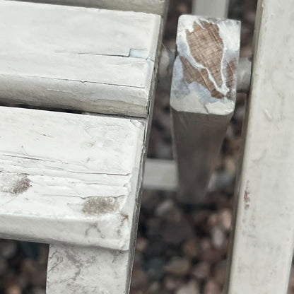 A close-up view of a painted wooden slatted garden chair set amidst a lush garden backdrop.