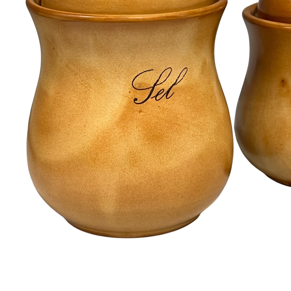 A close-up of a warm tan ceramic canister with a matching lid, featuring the black cursive script 'Sel' on the front, set against a plain white background with another canister partially visible on the right.