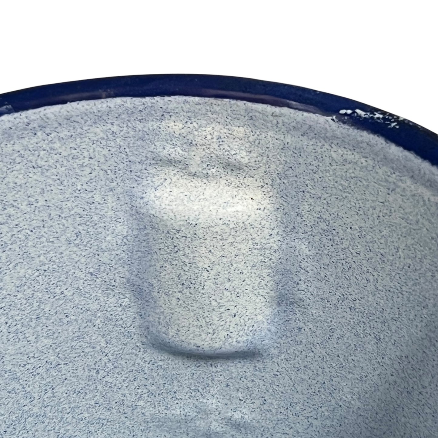 A close-up of a textured, speckled light gray surface with a dark blue rim, showing a soft reflection in the center.