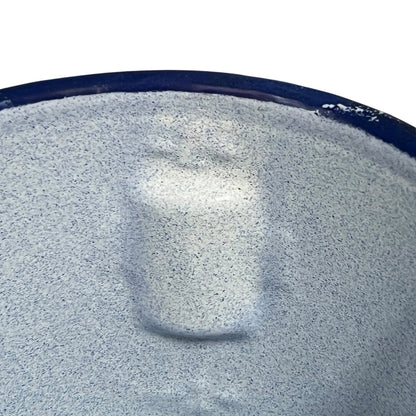 A close-up of a textured, speckled light gray surface with a dark blue rim, showing a soft reflection in the center.