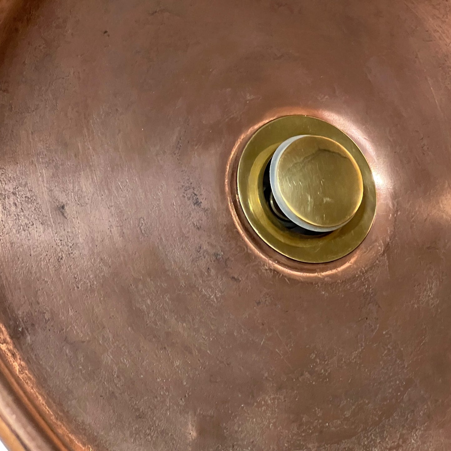 Close-up of a copper sink basin with a round brass drain assembly visible in the center.