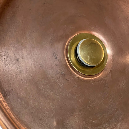 Close-up of a copper sink basin with a round brass drain assembly visible in the center.