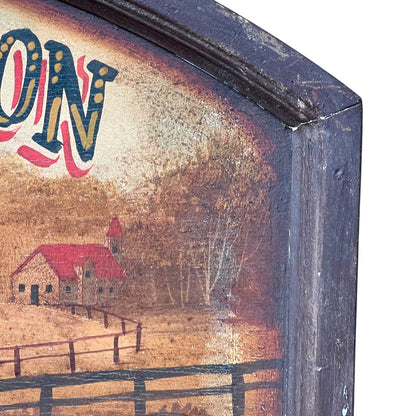 Close-up of a rustic painted wooden sign showing part of a farm scene with a red-roofed house, fence, trees, and distressed dark blue lettering on a cream background.