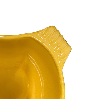 Close-up of a glossy mustard yellow ceramic bowl showing the textured rim against a plain white background.
